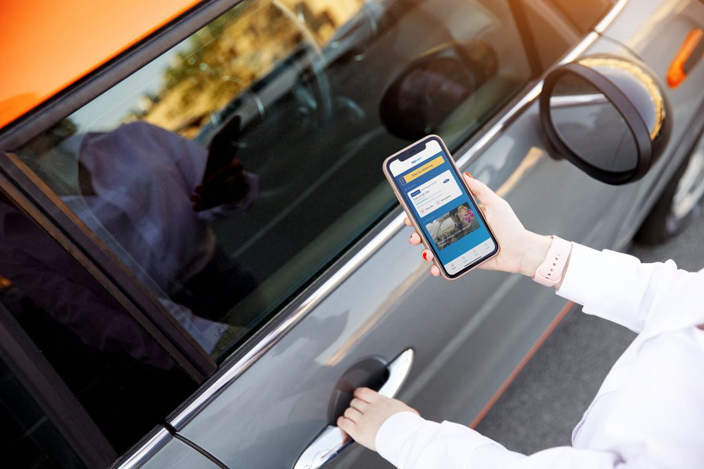 person holding mobile with hand on car door handle